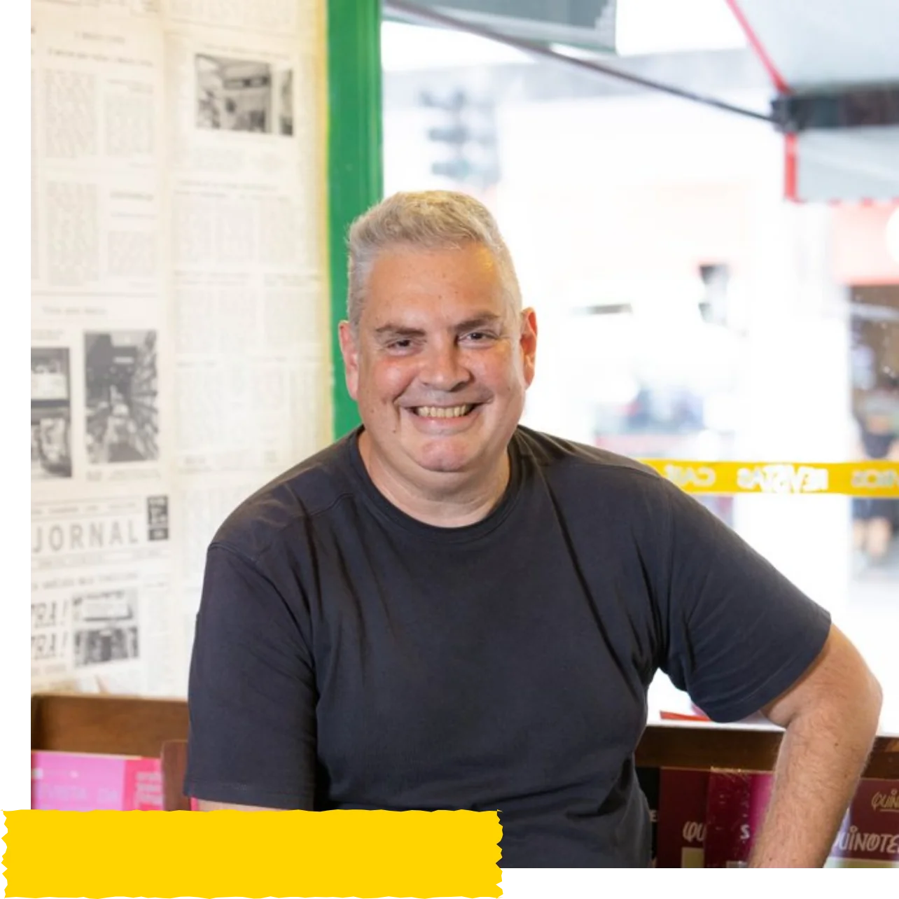 José Luiz Tahan sorrindo, sentado em uma livraria